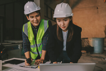 Construction manager and engineer dressed in orange work vests and hard helmets explore...