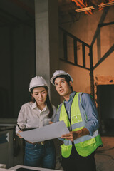 Construction manager and engineer dressed in orange work vests and hard helmets explore...