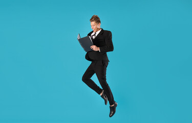 Businessman with folder jumping on light blue background