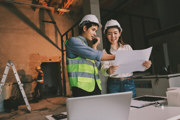 Construction manager and engineer dressed in orange work vests and hard helmets explore...