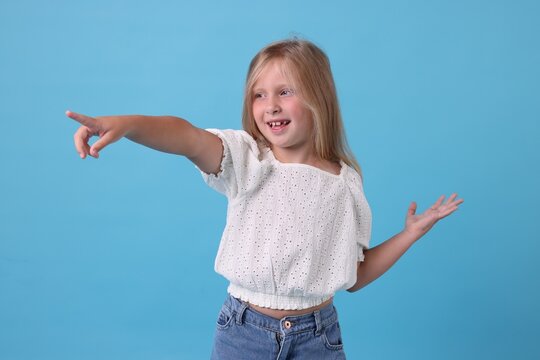 Cute little girl pointing at something and laughing on light blue background
