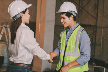 Construction manager and engineer dressed in orange work vests and hard helmets explore...