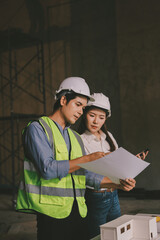 Construction manager and engineer dressed in orange work vests and hard helmets explore...