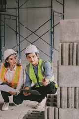 Construction manager and engineer dressed in orange work vests and hard helmets explore...