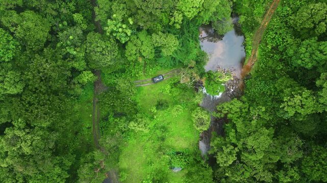 Aerial drone view of 900 Kandi in Wayanad, Kerala, during monsoon. Dense green forest surrounds a hidden natural pool while moving fog drifts through the trees.