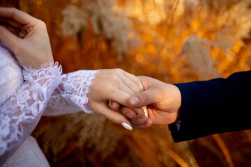 Close-up of two hands gently holding each other, woman in lace sleeve and man in suit, with autumn...