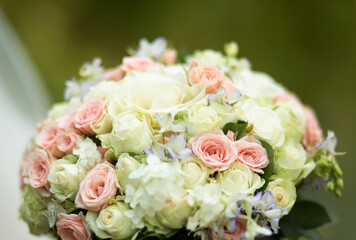 Close-up of a bouquet with white, cream and pink roses decorated with greenery and delicate flowers.