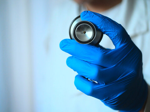 m&eacute;decin qui tient un st&eacute;thoscope (dans le mauvais sens) avec une blouse blanche et des gants bleus