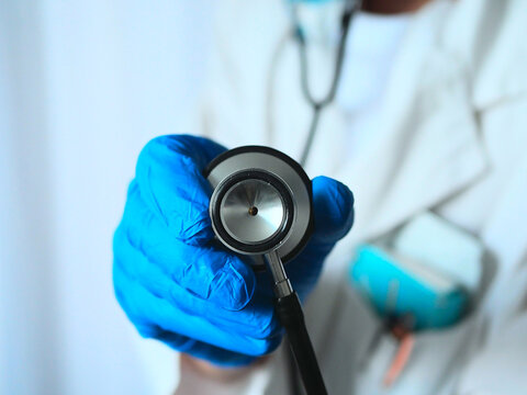 m&eacute;decin qui tient un st&eacute;thoscope (dans le mauvais sens) avec une blouse blanche et des gants bleus