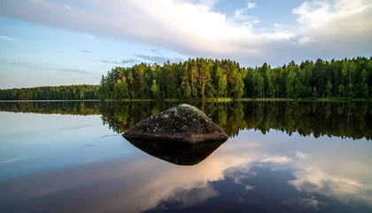 Tableau sur plexiglas Réflexion A tranquil lake scene at dawn, showcasing a large rock reflected perfectly in the still water, with lush forest lining the shore.  © rondaf