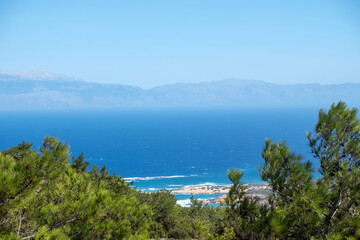 Naklejka premium Sarakiniko Beach on Gavdos Island, Greece, Turquoise rippled sea water, green pine trees and distant mountains under blue sky