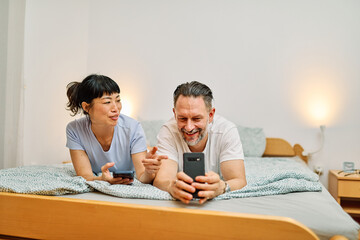 Portrait of a lovely young couple  or friends having fun together using a mobile phone in bed at home