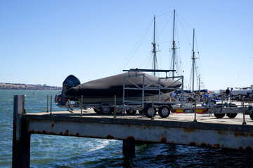 Boat on trailer at dock with sailboats in background under clear blue sky and calm water environment