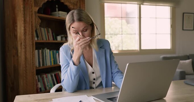 Fatigued woman working laptop, removes glasses, rubs bridge of nose, feels strain of long hours staring at screen. Burnout, deadlines, importance of taking breaks to maintain health and productivity