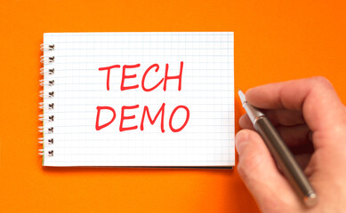 Tech demo symbol. Concept word Tech demo on beautiful white note. Businessman's hand with pen....