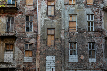 Wall of an abandoned building with boarded up windows stands in silence. Its windows sealed with...