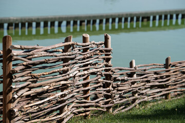 Rustic wooden wattle fence by the lake. Traditional handmade fence made of intertwined branches,...