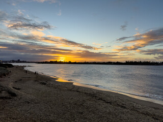 Scenic view of the sun setting over Stockton Beach with people walking along the shoreline,...