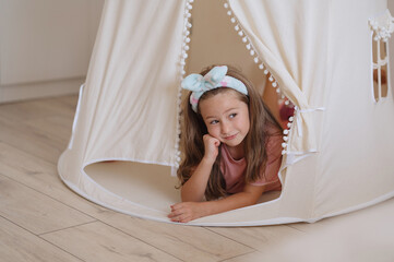 A cute girl is playing in a baby tent with soft colors. A happy childhood. Girlishness
