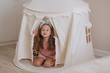 A cute girl is playing in a baby tent with soft colors. A happy childhood. Girlishness