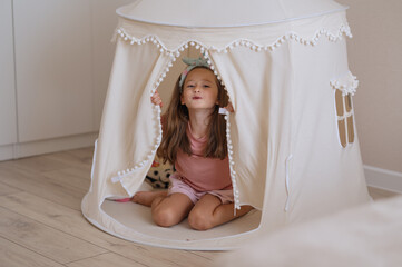 A cute girl is playing in a baby tent with soft colors. A happy childhood. Girlishness