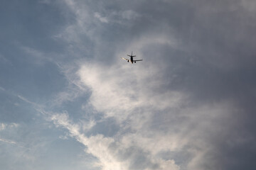 An airplane flies overhead, framed by a dramatic sky filled with billowing clouds. The contrast between metal and mist creates a striking visual of technology meeting nature.