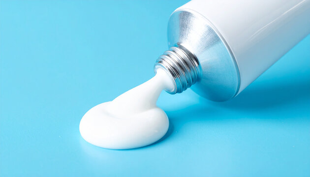 Metal tube squeezing white cream onto white background. Dermatology and skincare product.