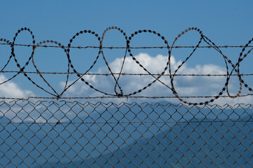 Barbed wire fence on blue sky background. Conceptual photo of security. Barbed wire fence in front of a blue sky with mountains and clouds