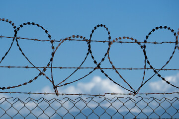Barbed wire fence on blue sky background. Conceptual photo of security. Barbed wire fence in front...