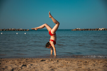 Energetic teenager girl doing handstand on the beach