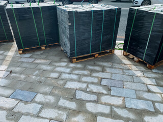 Pallets filled with various construction materials have been neatly arranged on a paved surface,...