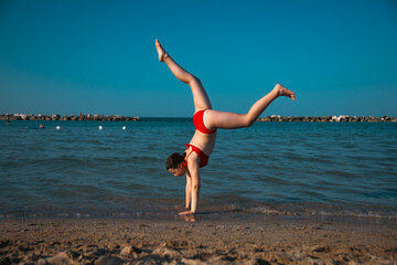Energetic teenager girl doing handstand on the beach