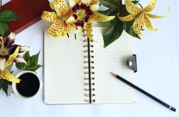 Notebook with pen, coffee and flowers on a white background.