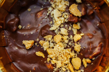 Close up of creamy chocolate dessert topped with crushed nuts in golden wrapper on purple background