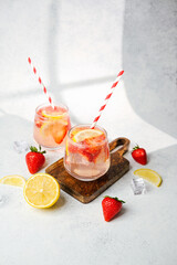 Strawberry lemon sparkling drink in round glasses with red striped straws on wooden board