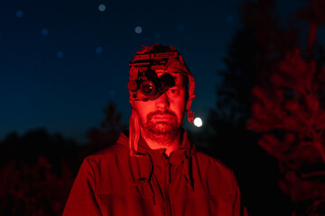 Portrait of a man wearing tactical headgear with a night vision device, illuminated by red light...