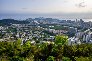 A panoramic view of Sanya, Hainan, China with numerous buildings, a winding river, and mountains in...
