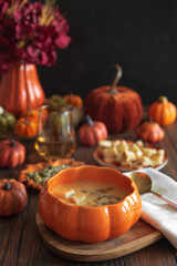 Creamy pumpkin soup with croutons and seeds, served in a pumpkin-shaped bowl on dark wooden table.