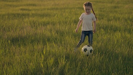 Little child runs across the green football field playing football at sunset in the sky, kid kicks...