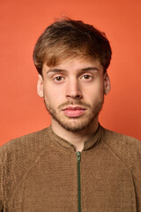 Young Caucasian man looking directly into camera with serious expression on orange background