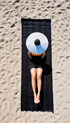 Woman sunbathing on beach wearing large hat and black outfit.