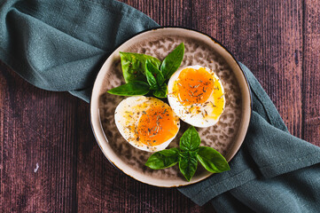 Close up of soft-boiled egg split in half with spices and basil leaves on a plate on a table top view