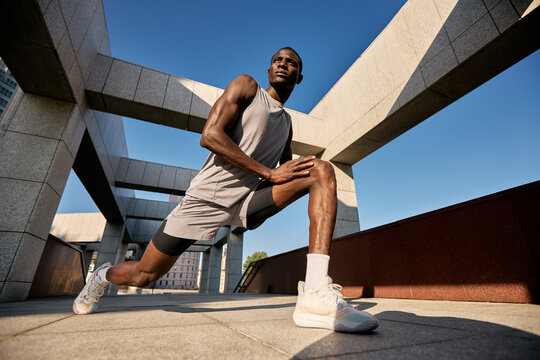 Athletic man stretching outdoors in urban setting on a sunny day