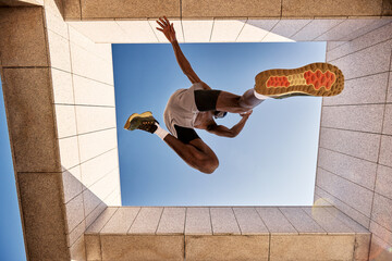 Dynamic low angle shot of man leaping under clear blue sky outdoors