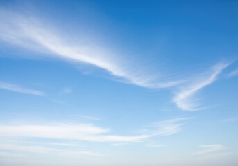 Obraz premium Wispy white clouds drift across a vast, clear blue sky on a bright, sunny day, creating a serene and peaceful atmosphere