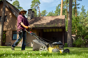 Man mowing lawn in a garden with a modern yellow lawnmower on a sunny day