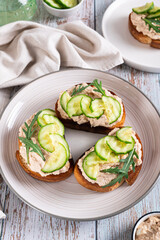 Homemade toasts with cod liver, cucumber and herbs on a plate on a table vertical view
