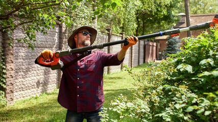 Man trimming garden hedges with powered tool on a sunny day outdoors