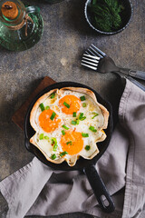 Fried eggs with green onions in a tortilla on a frying pan on the table top and vertical view
