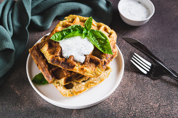 Zucchini waffles with spices, sour cream and herbs on a plate on the table